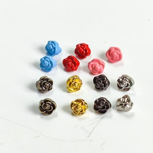 Puede incluir: Surtido de botones con forma de rosa en varios colores, incluyendo azul, rojo, rosa, dorado, plateado y negro.