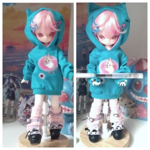 May include: A turquoise hooded sweatshirt with a pink cat graphic and the text "I love you most" on a doll with pink hair and white boots.