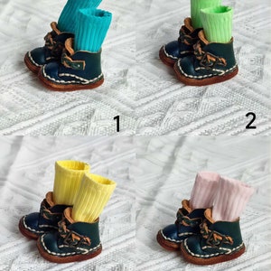 May include: Four pairs of miniature leather boots with different colored socks. The boots are dark blue with brown leather accents and laces. The socks are turquoise, light green, yellow, and pink.