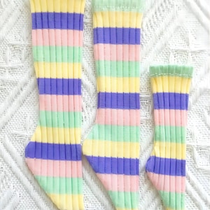 Pode incluir: Tr&ecirc;s pares de meias listradas em cores pastel, incluindo rosa, amarelo, verde e roxo. As meias est&atilde;o dispostas em uma fila do maior para o menor.