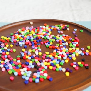 Puede incluir: Una bandeja de madera llena de botones de plástico de colores. Los botones son pequeños y redondos, y están esparcidos al azar por la bandeja.
