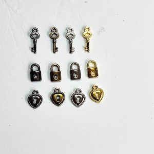 Puede incluir: Surtido de dijes de llave en oro y plata, incluyendo dijes de cerradura con ojo de cerradura y dijes de cerradura en forma de corazón.