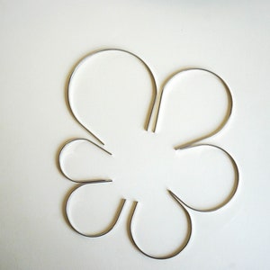 Pu&ograve; includere: Sei cerchietti per capelli in metallo argentato disposti a forma di fiore su una superficie bianca.