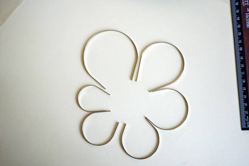 Pu&ograve; includere: Sei cerchietti per capelli in metallo argentato disposti a forma di fiore su una superficie bianca.