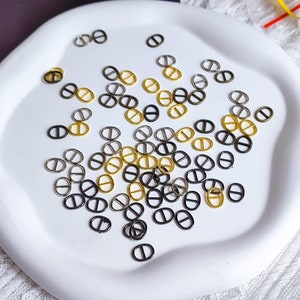 Peut inclure: Une assiette blanche avec une variété d'anneaux en métal dorés et noirs. Les anneaux sont tous de la même forme, mais de tailles différentes. Ils sont disposés de manière aléatoire sur l'assiette.