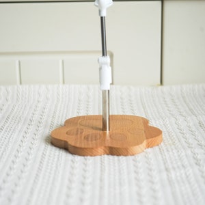 May include: A wooden paw-shaped stand with a metal rod and a white plastic top. The stand is designed to hold a mug or cup.