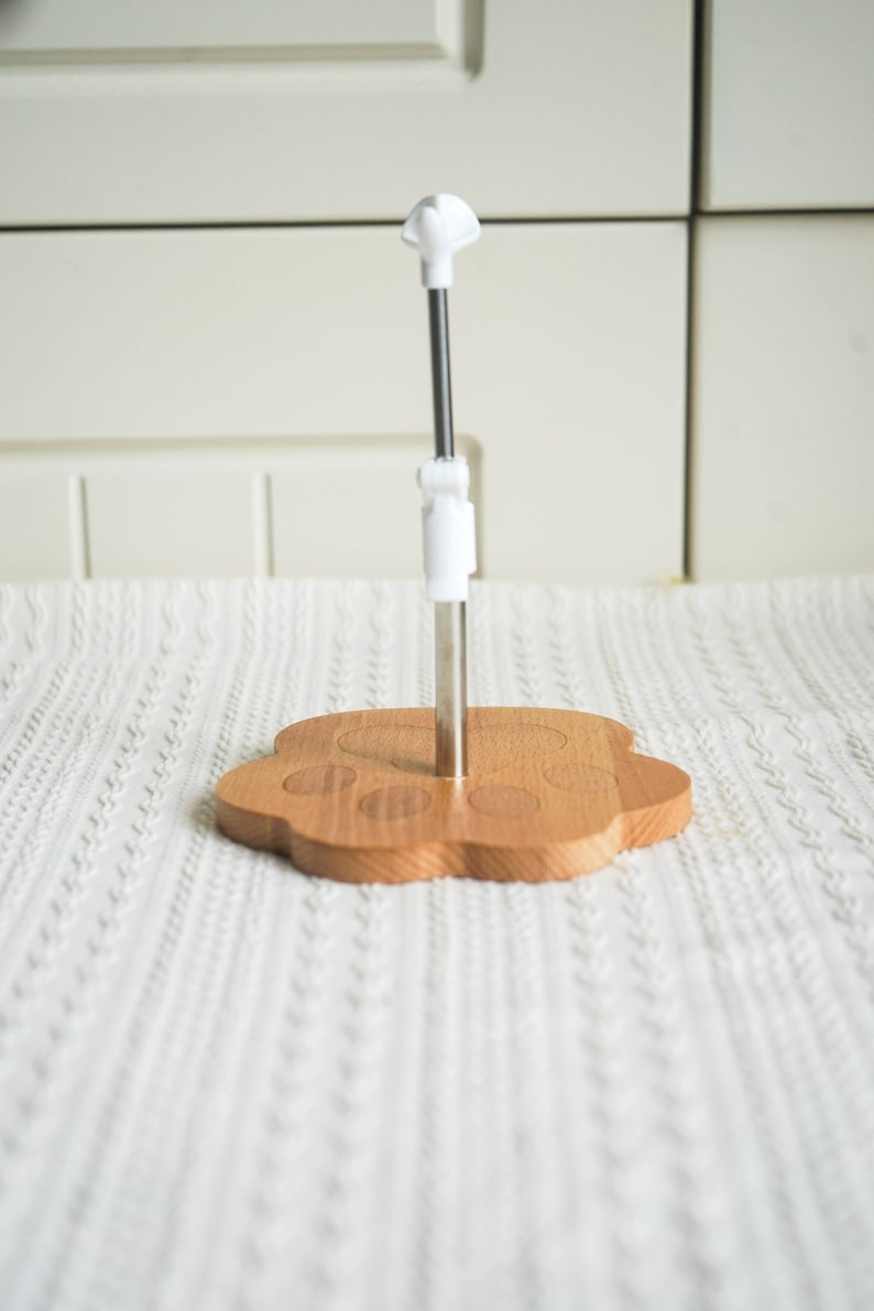 May include: A wooden paw-shaped stand with a metal rod and a white plastic top. The stand is designed to hold a mug or cup.
