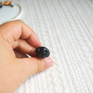 May include: A black plastic button shaped like a cartoon nose with two small black circles for nostrils.