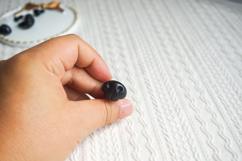 May include: A black plastic button shaped like a cartoon nose with two small black circles for nostrils.