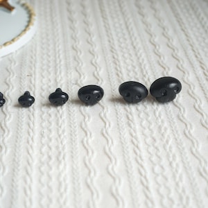 May include: A set of six black plastic safety eyes for crafts. The eyes are arranged in order of size, from smallest to largest.