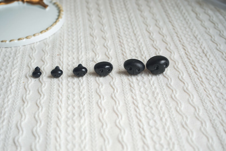 May include: A set of six black plastic safety eyes for crafts. The eyes are arranged in order of size, from smallest to largest.