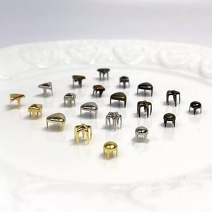 Könnte beinhalten: Sortiment aus Metallnieten in verschiedenen Formen und Größen, darunter Sterne, Herzen und Dreiecke. Die Nieten sind in Silber, Gold und Schwarz.