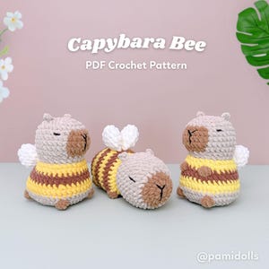 May include: Three crocheted capybara bee plushies. The capybaras are light brown and tan with yellow and brown striped bee bodies. The text "Capybara Bee PDF Crochet Pattern" is at the top of the image.