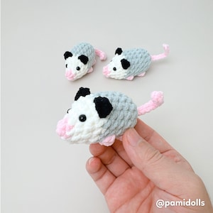 K&ouml;nnte beinhalten: Drei geh&auml;kelte Opossums. Die Opossums haben graue K&ouml;rper, schwarze Ohren und rosa Nasen und Schw&auml;nze. Ein Opossum wird von einer Hand gehalten. Das Bild hat den Text "@pamidolls" in der unteren rechten Ecke.