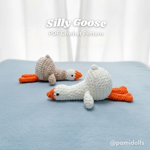 Puede incluir: Dos juguetes de ganso de ganchillo, uno beige y otro blanco, con patas y picos naranjas, yacen sobre una superficie azul. El texto "Silly Goose PDF Crochet Pattern" se muestra encima de los juguetes. Los juguetes están hechos a mano.