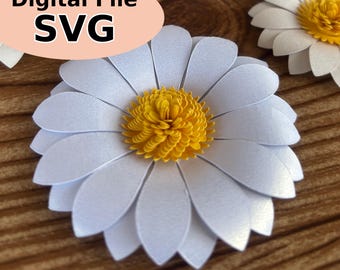 Op de afbeelding: Close-up van een witte papieren madeliefbloem met een gele kern. De bloemblaadjes zijn gelaagd. De afbeelding bevat de tekst "Digital File SVG" in een roze ovaal.