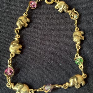 May include: A gold-tone chain bracelet featuring alternating metal elephant charms and small faceted crystal beads in pink, green, and clear hues. The bracelet is secured with a circular spring ring clasp and consists of six elephant charms.