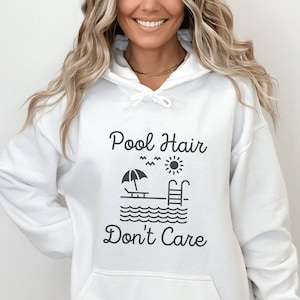 May include: White hooded sweatshirt with the text "Pool Hair Don't Care" in black lettering. A small graphic of a pool with a sun, an umbrella, and a lounge chair is above the text.