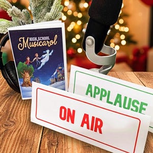 May include: A festive scene with a microphone, headphones, and signs reading "ON AIR" and "APPLAUSE." A book titled "High School Musicalcarol" is propped up with a Christmas tree branch. The background features a blurred Christmas tree and presents.