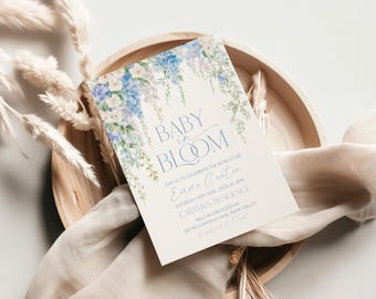 Puede incluir: Una invitación a un baby shower con un diseño floral de acuarela en tonos azules y blancos. El texto dice "Baby in Bloom" e incluye el nombre "Enne Carter" y la fecha "Sábado 18 de junio de 2025 a las 3 pm". La invitación también incluye la ubicación "Carter's Residence, Willow Creek Estate, 267 Bloomfield Lane, Napa Valley".