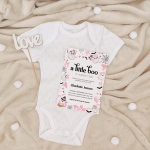 Puede incluir: Un body blanco para beb&eacute; con una invitaci&oacute;n de baby shower rosa y negra que dice "a little boo is almost due". La invitaci&oacute;n tiene un lindo dise&ntilde;o de fantasma y murci&eacute;lago.