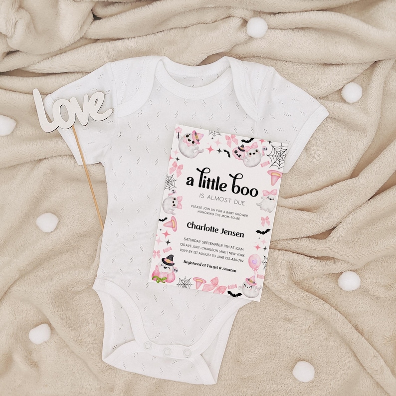 Puede incluir: Un body blanco para beb&eacute; con una invitaci&oacute;n de baby shower rosa y negra que dice "a little boo is almost due". La invitaci&oacute;n tiene un lindo dise&ntilde;o de fantasma y murci&eacute;lago.