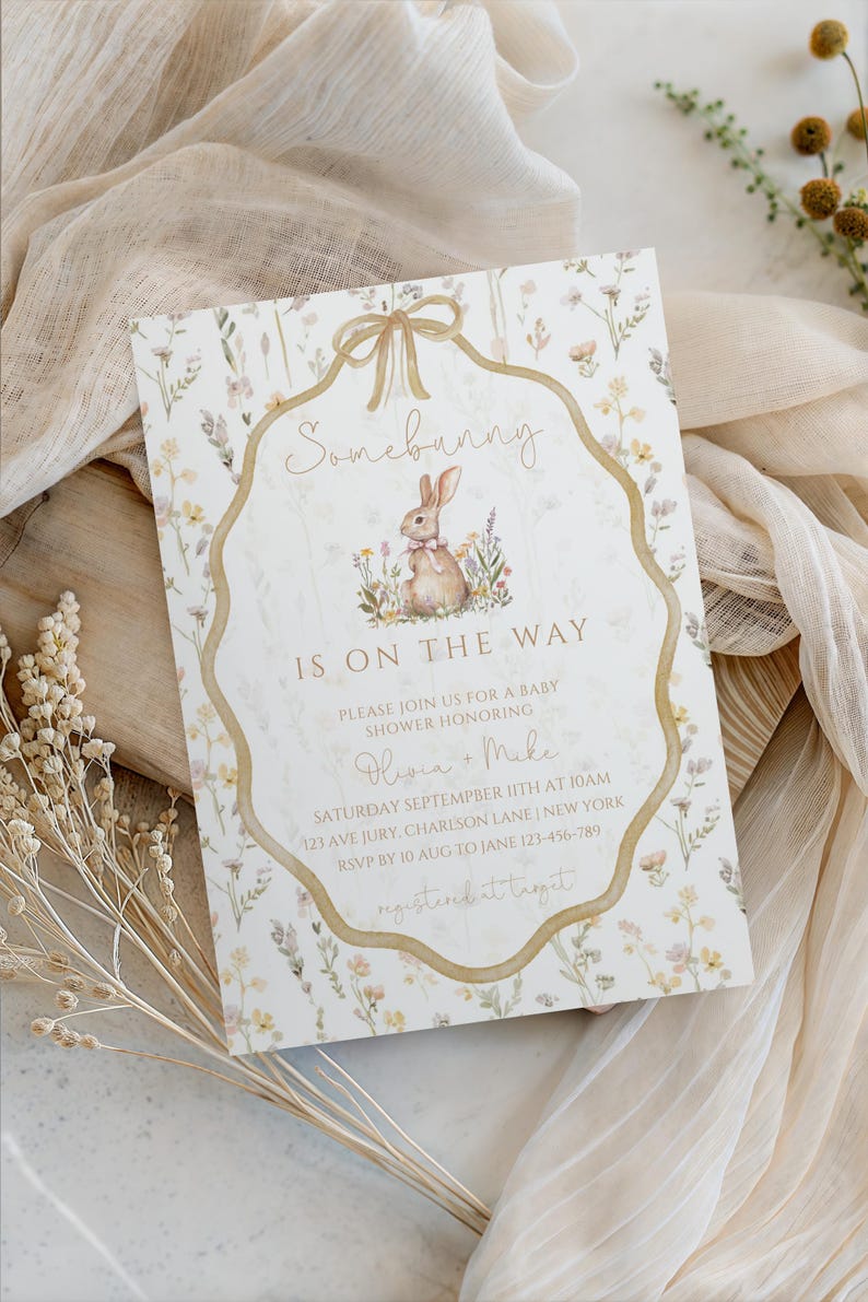 May include: Baby shower invitation with a floral design and a watercolor illustration of a bunny. The invitation features the text "Somebunny is on the way" and event details. The invitation is decorated with a gold ribbon and floral accents.