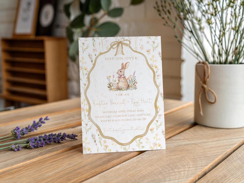 May include: An Easter-themed invitation card with a bunny illustration. The card features floral accents and the text "Hop-On-Over" and "Easter Bread & Egg Hunt". The invitation is on a wooden surface.