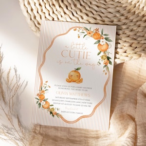 May include: Baby shower invitation with the text "a little cutie is on the way." The invitation features an orange illustration and floral accents. The invitation is on a striped background.