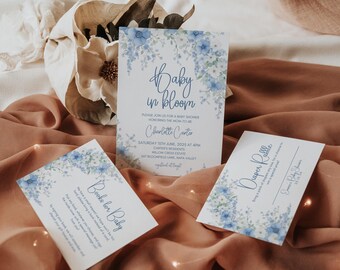 Op de afbeelding: Drie babyborrelkaarten met een blauw bloemenontwerp. De hoofkaart zegt "Baby in Bloom" en bevat de tekst "Sluit je aan bij ons voor een babyborrel ter ere van de aanstaande mama Charlotte Cartie". De tweede kaart zegt "Boeken voor Baby" en de derde kaart zegt "Luierspel".