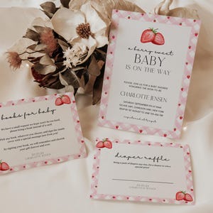 May include: Pink and white baby shower invitation with a strawberry design. The invitation says "a berry sweet baby is on the way" and includes the name Charlotte Jensen. There are also cards for a diaper raffle and a book request for the baby.