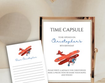 Puede incluir: Un letrero con marco dorado y una tarjeta con una ilustración de avión rojo. El letrero dice "TIME CAPSULE" y "Christopher's 18th Birthday". La tarjeta dice "Dear Christopher" y tiene líneas para escribir.