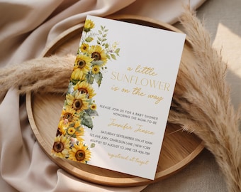 May include: Baby shower invitation with a sunflower design. The invitation has a watercolour design of sunflowers and foliage on the left. Gold script reads "a little sunflower is on the way". The invitation also includes the mom-to-be's name, date, time, and location.
