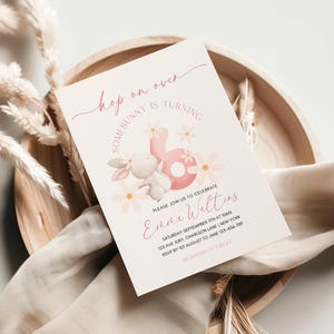 以下が含まれることがあります： ピンクと白の招待状で、ウサギのイラストと「Hop on over Somebunny is turning」と「Enna Walters」のテキストが書かれています。招待状には誕生日パーティーの詳細が記載されています。
