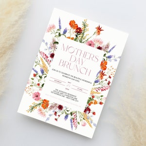 Pu&ograve; includere: Un invito per un brunch della festa della mamma con bordo floreale. L'invito presenta il testo "Mothers Day Brunch". L'invito include la data, l'ora e il luogo dell'evento. Il bordo floreale comprende fiori arancioni, rosa e viola.