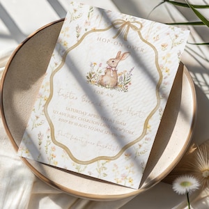 May include: An Easter brunch and egg hunt invitation card with a watercolor bunny illustration. The invitation is on a cream-colored background with floral accents and the text "Hop-On-Over". The card is on a beige plate.