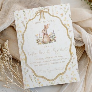 May include: An Easter brunch and egg hunt invitation with a watercolor illustration of a bunny surrounded by flowers. The invitation has a gold border and a bow at the top, with the text "Hop-On-Over".