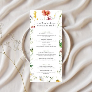 Pode incluir: Um menu de brunch do Dia das Mães com detalhes florais em aquarela. O menu apresenta entradas como torrada de abacate e salmão defumado e mini quiches, pratos principais como ovos Benedict e fritatta de espinafre e sobremesas.