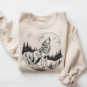 May include: A beige sweatshirt featuring a black and white graphic print of a wolf howling at the moon in a forest setting.