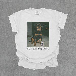 T-shirt featuring a retro-style photo of an unbothered Rottweiler sitting on a porch with humorous meme energy and the caption ‘I Got That Dog In Me'