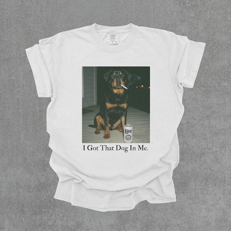 T-shirt featuring a retro-style photo of an unbothered Rottweiler sitting on a porch with humorous meme energy and the caption ‘I Got That Dog In Me'