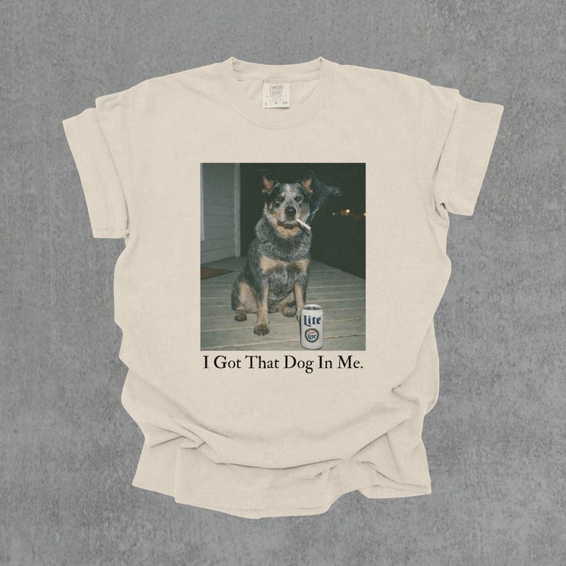 T-shirt featuring a retro-style photo of an unbothered australian cattle dog sitting on a porch with humorous meme energy and the caption ‘I Got That Dog In Me'