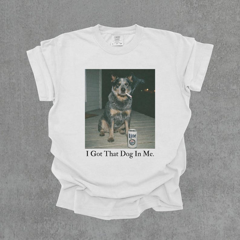 T-shirt featuring a retro-style photo of an unbothered australian cattle dog sitting on a porch with humorous meme energy and the caption ‘I Got That Dog In Me'