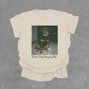 T-shirt featuring a retro-style photo of an unbothered Rottweiler sitting on a porch with humorous meme energy and the caption ‘I Got That Dog In Me'