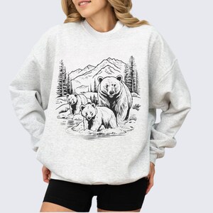 May include: A gray sweatshirt with a black and white illustration of three bears in a mountain landscape. The bears are standing in a stream of water.