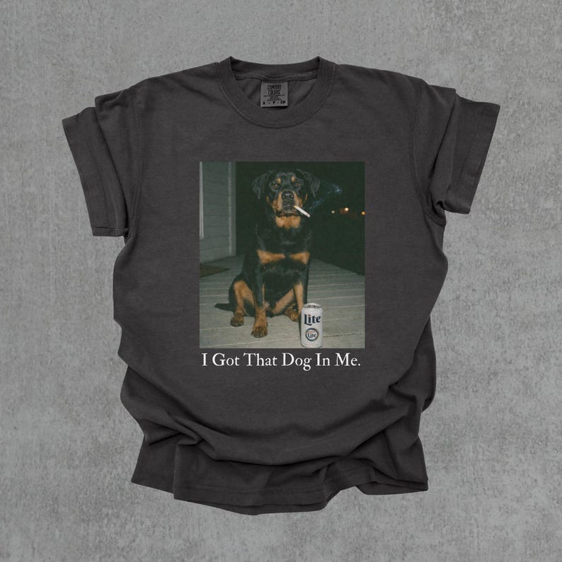 T-shirt featuring a retro-style photo of an unbothered Rottweiler sitting on a porch with humorous meme energy and the caption ‘I Got That Dog In Me'