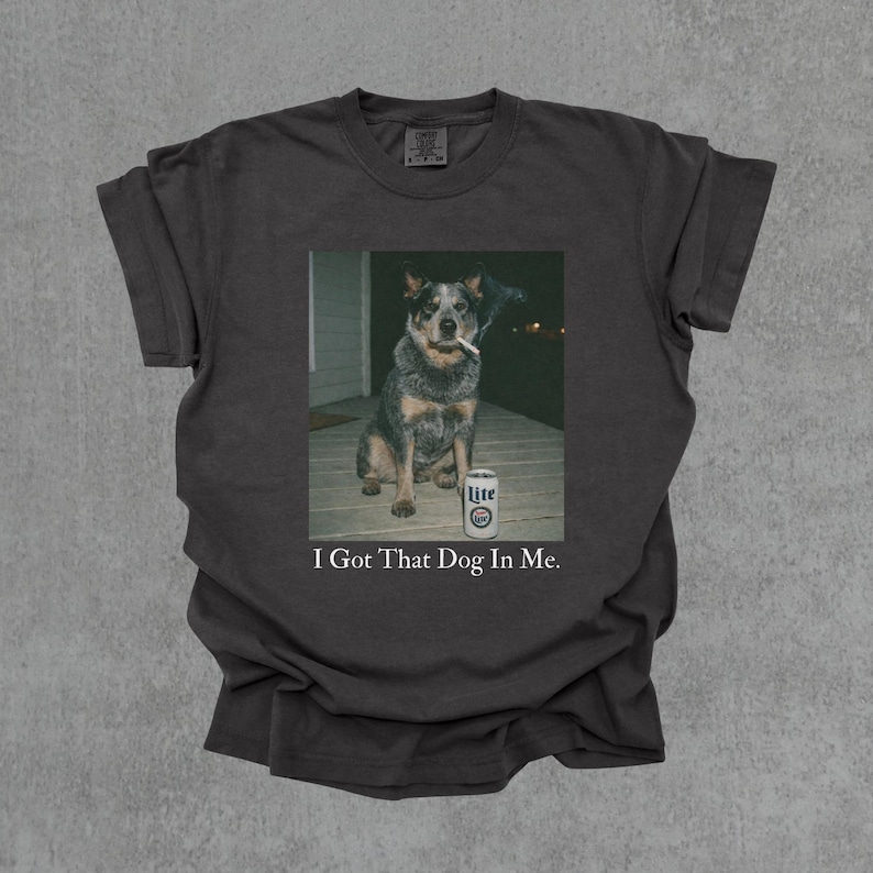 T-shirt featuring a retro-style photo of an unbothered australian cattle dog sitting on a porch with humorous meme energy and the caption ‘I Got That Dog In Me'