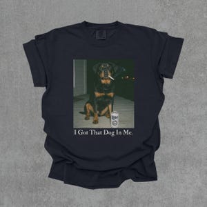 T-shirt featuring a retro-style photo of an unbothered Rottweiler sitting on a porch with humorous meme energy and the caption ‘I Got That Dog In Me'