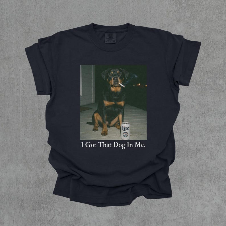T-shirt featuring a retro-style photo of an unbothered Rottweiler sitting on a porch with humorous meme energy and the caption ‘I Got That Dog In Me'
