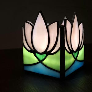 May include: A stained glass candle holder with a white lotus flower design. The holder has green and blue glass accents.